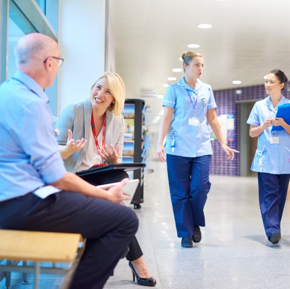A business woman chats to a doctor in a busy hospital corridor.