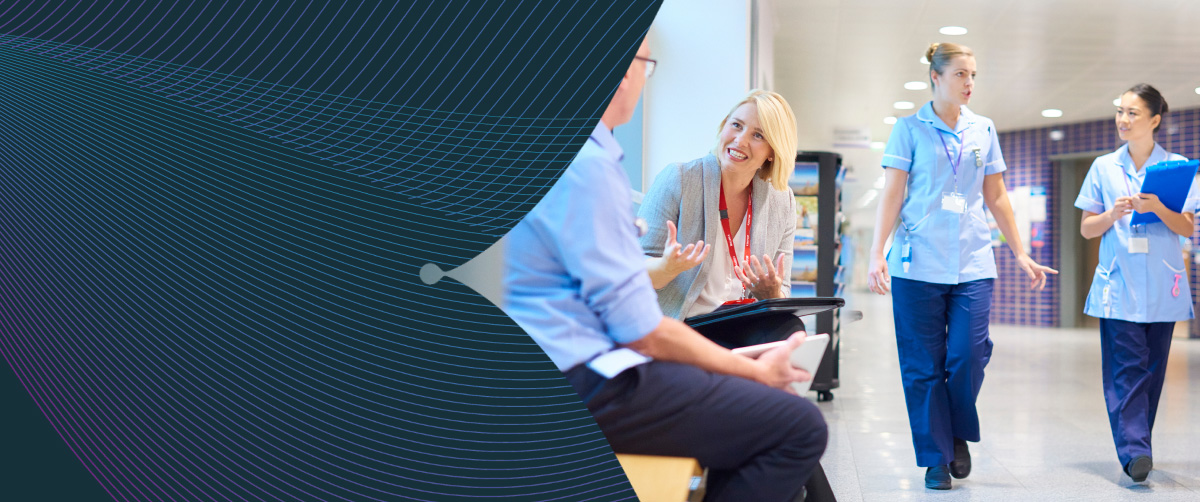 A business woman chats to a doctor in a busy hospital corridor.